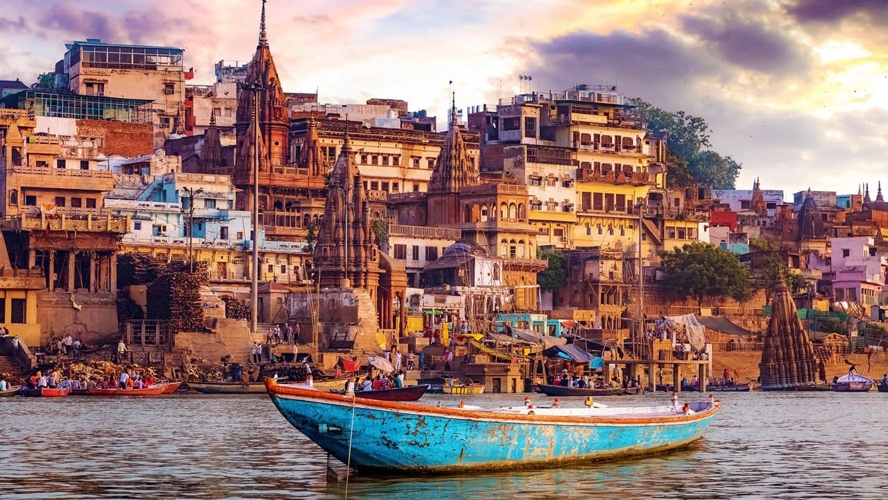 Varanasi ghats at golden hour: boats on the Ganges, pilgrims along the riverbank, temples and spires above the waterfront